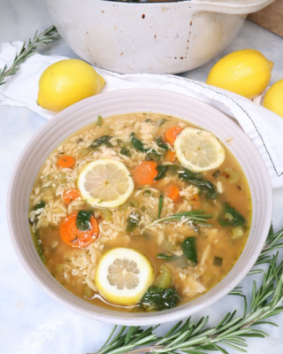 A steaming bowl of Lemon Chicken Orzo Soup filled with tender shredded chicken, vibrant spinach, carrots, celery, and golden orzo pasta, garnished with fresh dill and a slice of lemon.