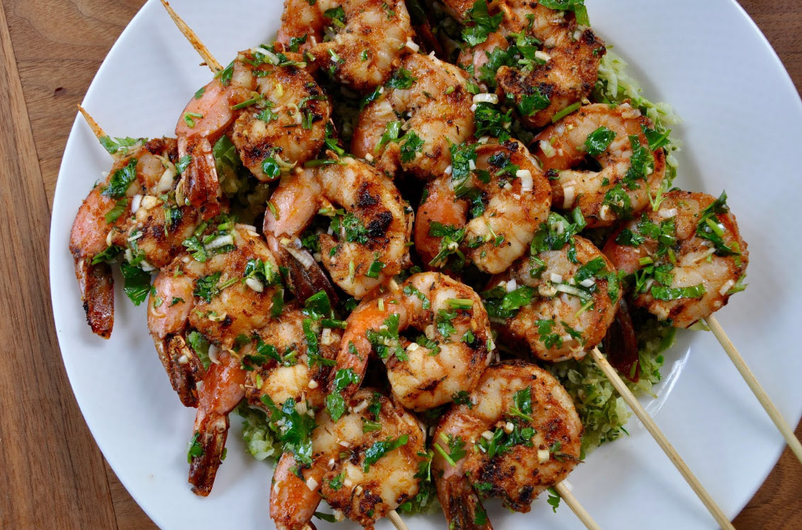 Grilled Cajun shrimp skewers with cilantro dressing on a plate, garnished with fresh herbs.