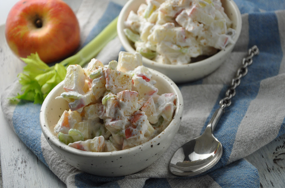 Creamy apple celery salad with yogurt dressing in a bowl, garnished with cinnamon and raisins.