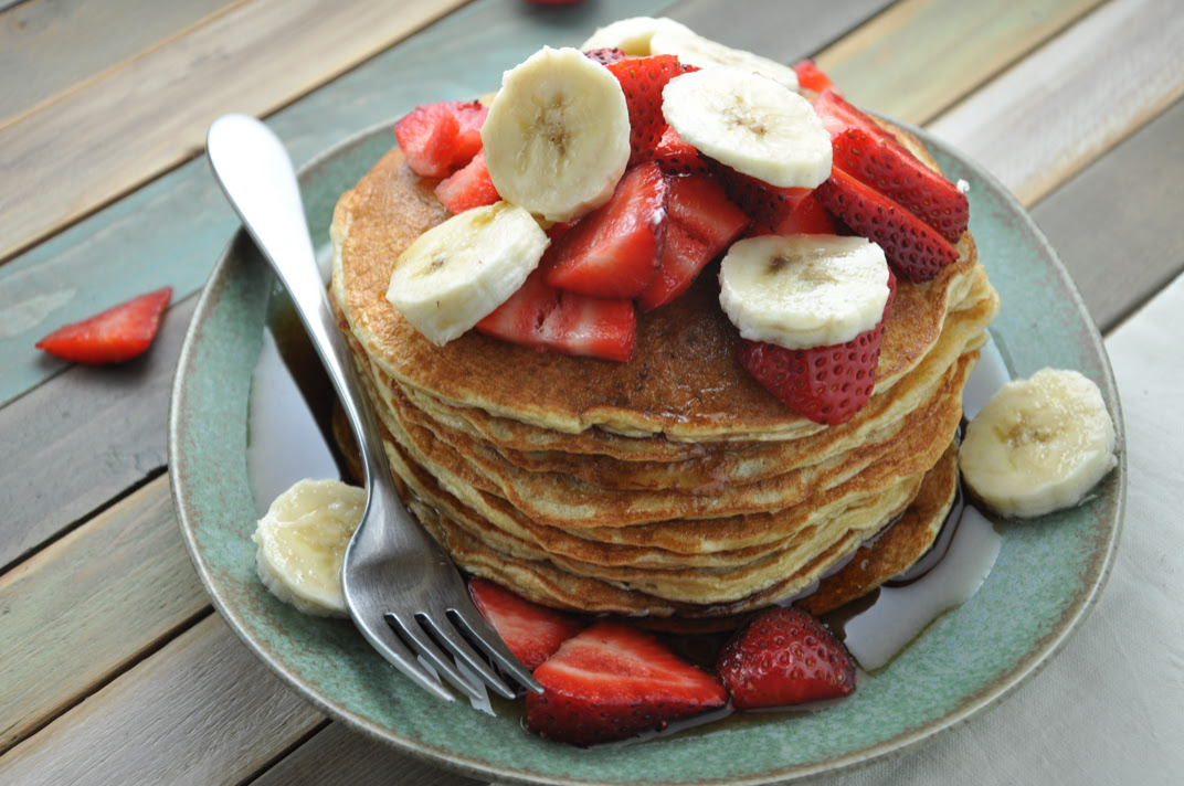 A stack of protein pancakes topped with fresh fruit and a drizzle of maple syrup.