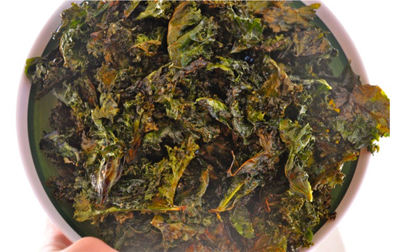A close-up of crispy homemade kale chips on a baking sheet, lightly seasoned and golden green, ready to be enjoyed as a healthy snack.