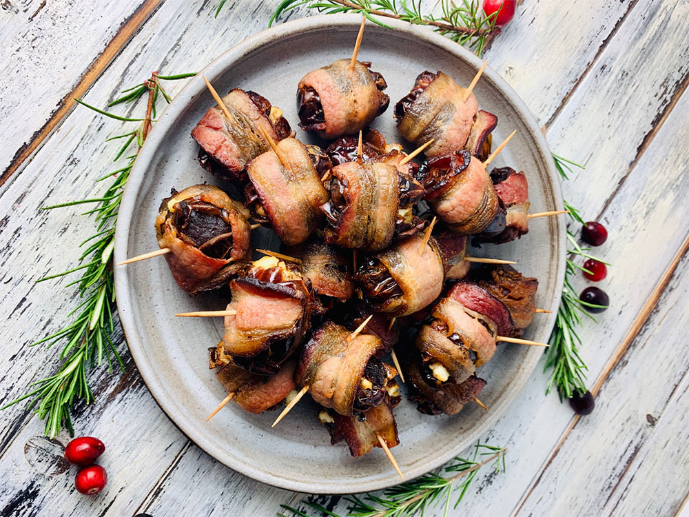 Bacon-wrapped stuffed dates filled with goat cheese and walnuts, arranged on a baking sheet.