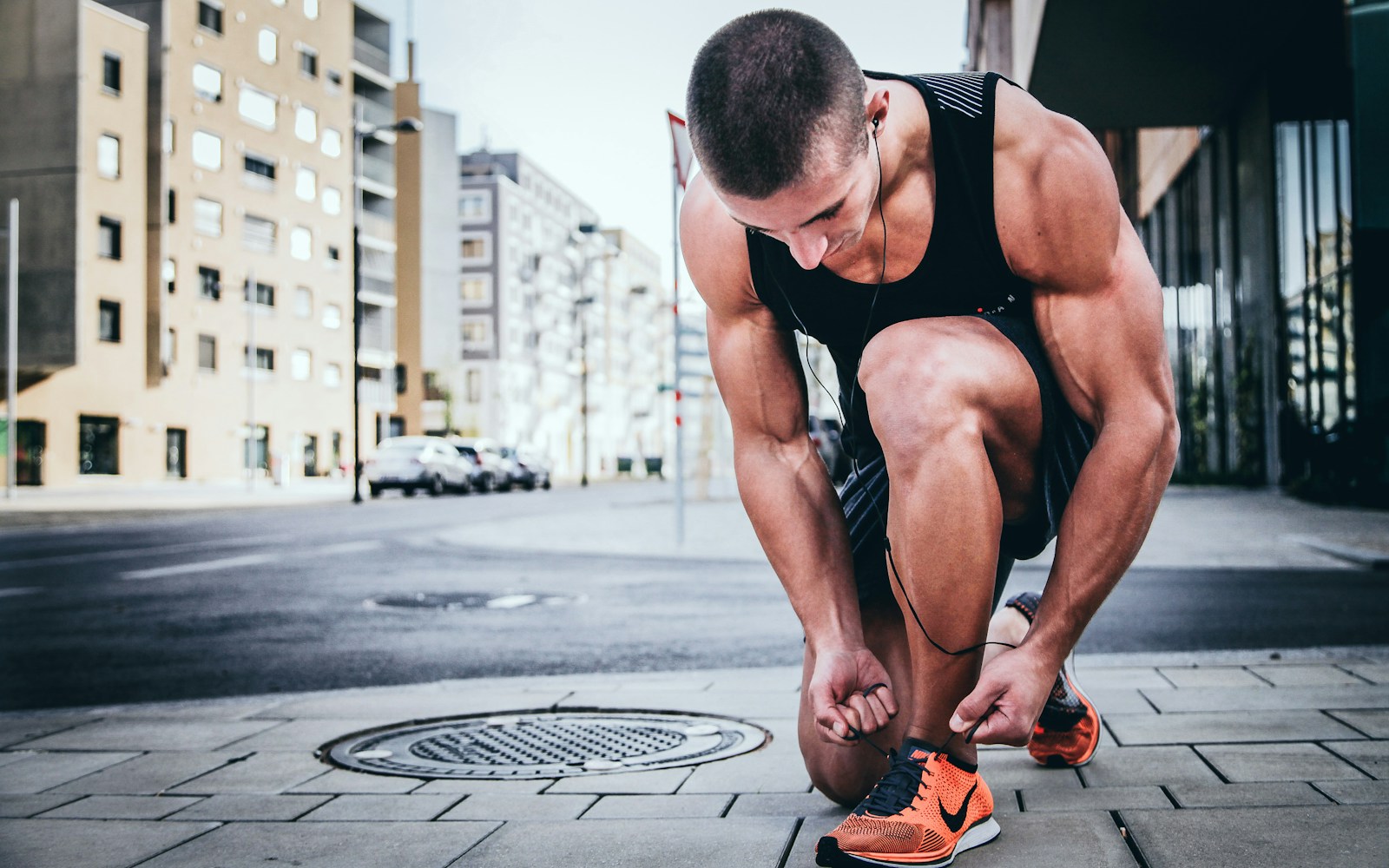 A man tying his running shoe, preparing for a workout, with a determined expression in a brightly lit outdoor setting.