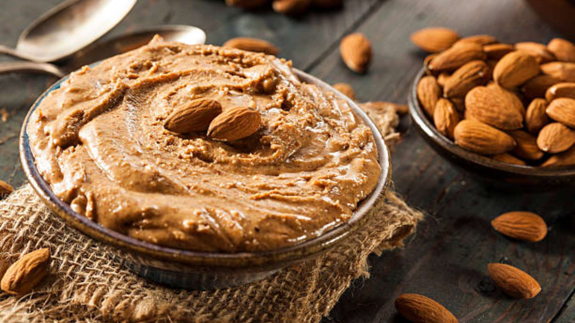 Jar of creamy homemade almond butter with almonds and sea salt beside it