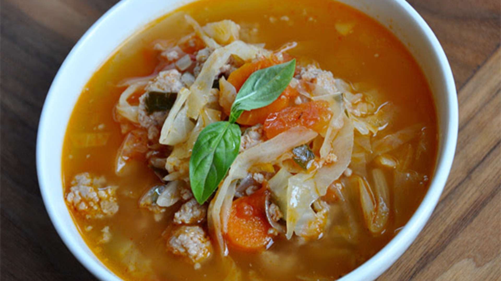 A bowl of cozy sausage and cabbage soup served with fresh herbs.